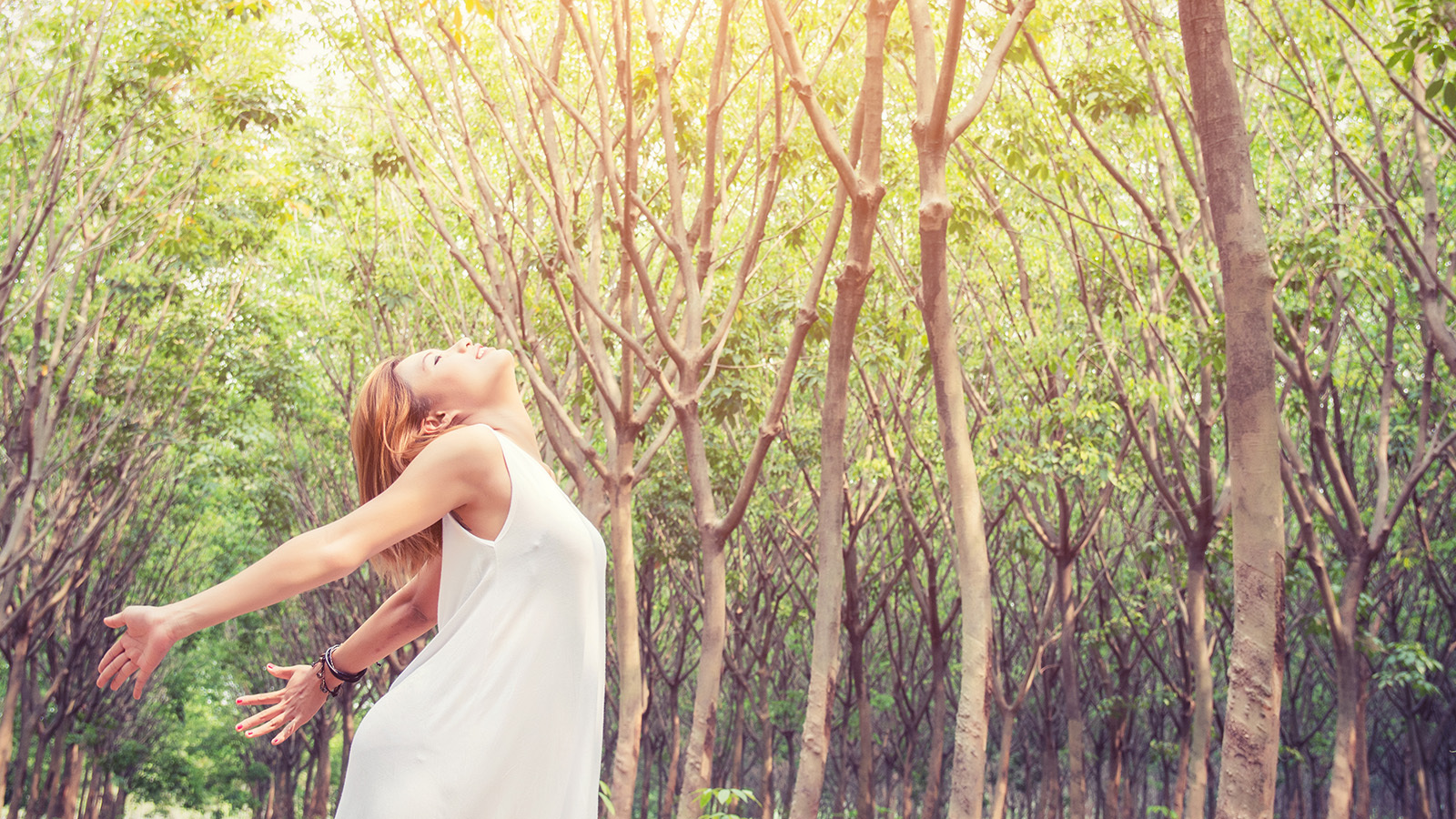 young woman breathes in the outdoor air surrounded by trees
