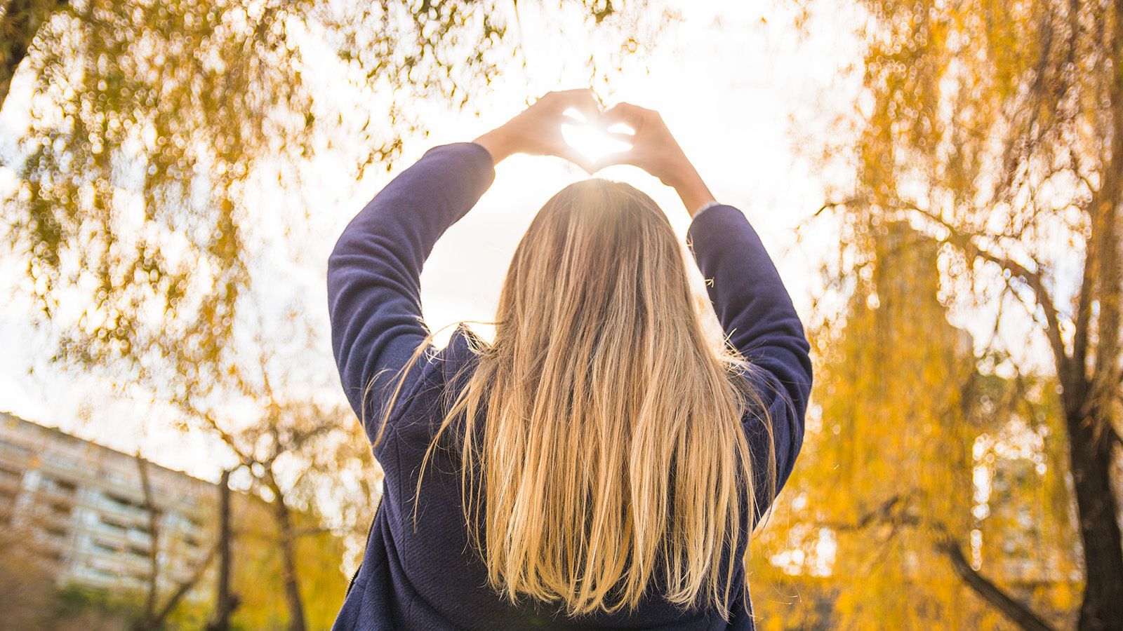 A woman makes a heart symbol with her hands around the sun
