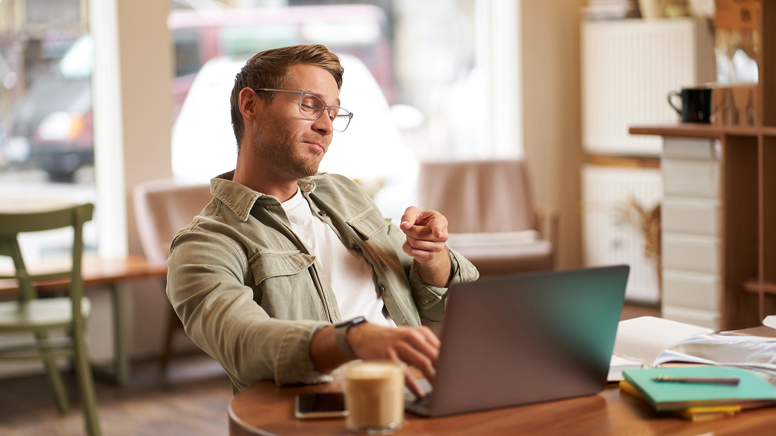 A satisfied man points to his laptop screen as he's working an a coffee shop