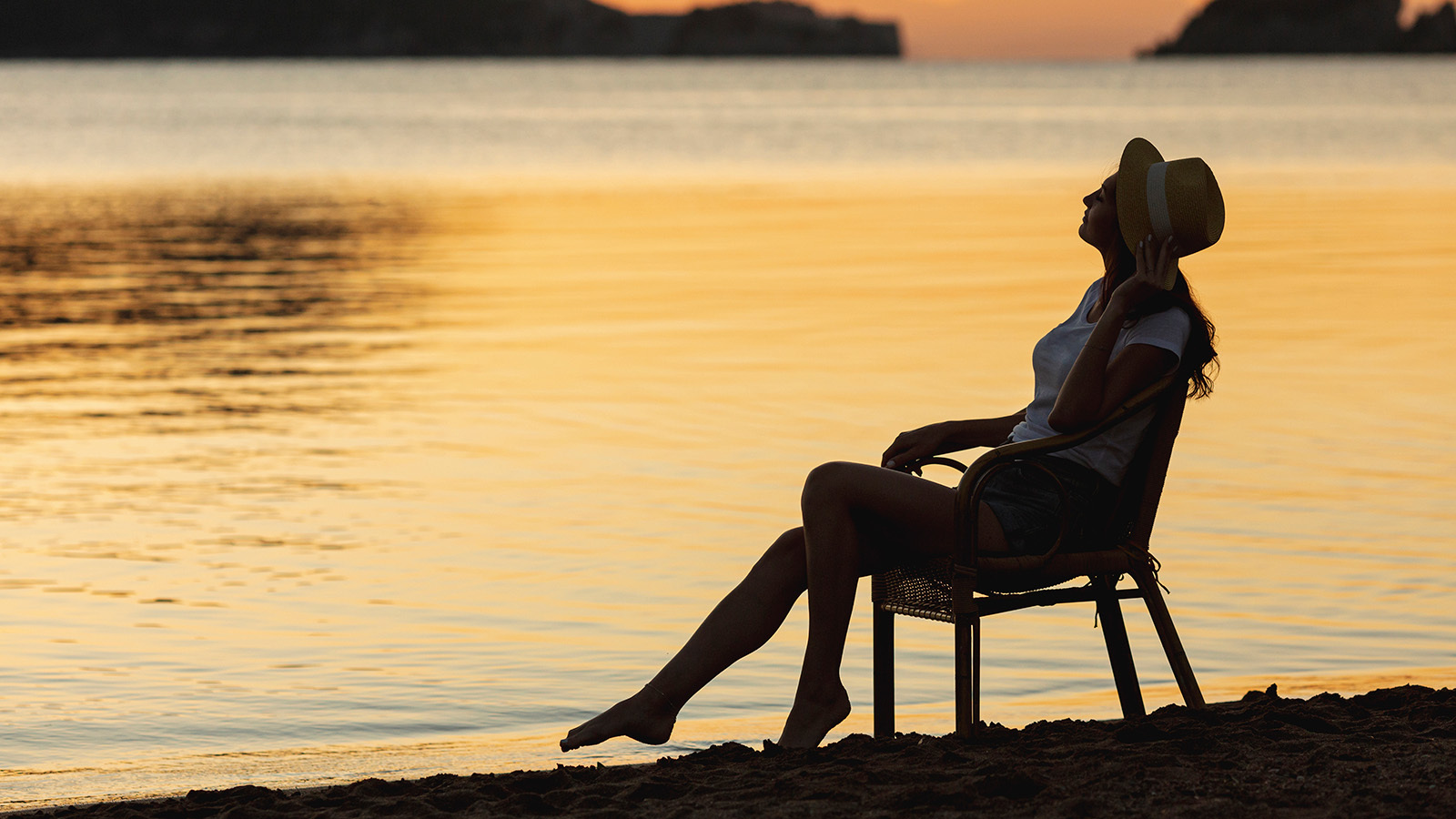 A woman relaxed in a chair next to a lake while the sun sets